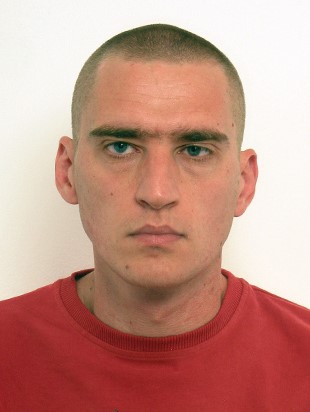 Portrait of a man with completely cropped hair, blue eyes and a red shirt.