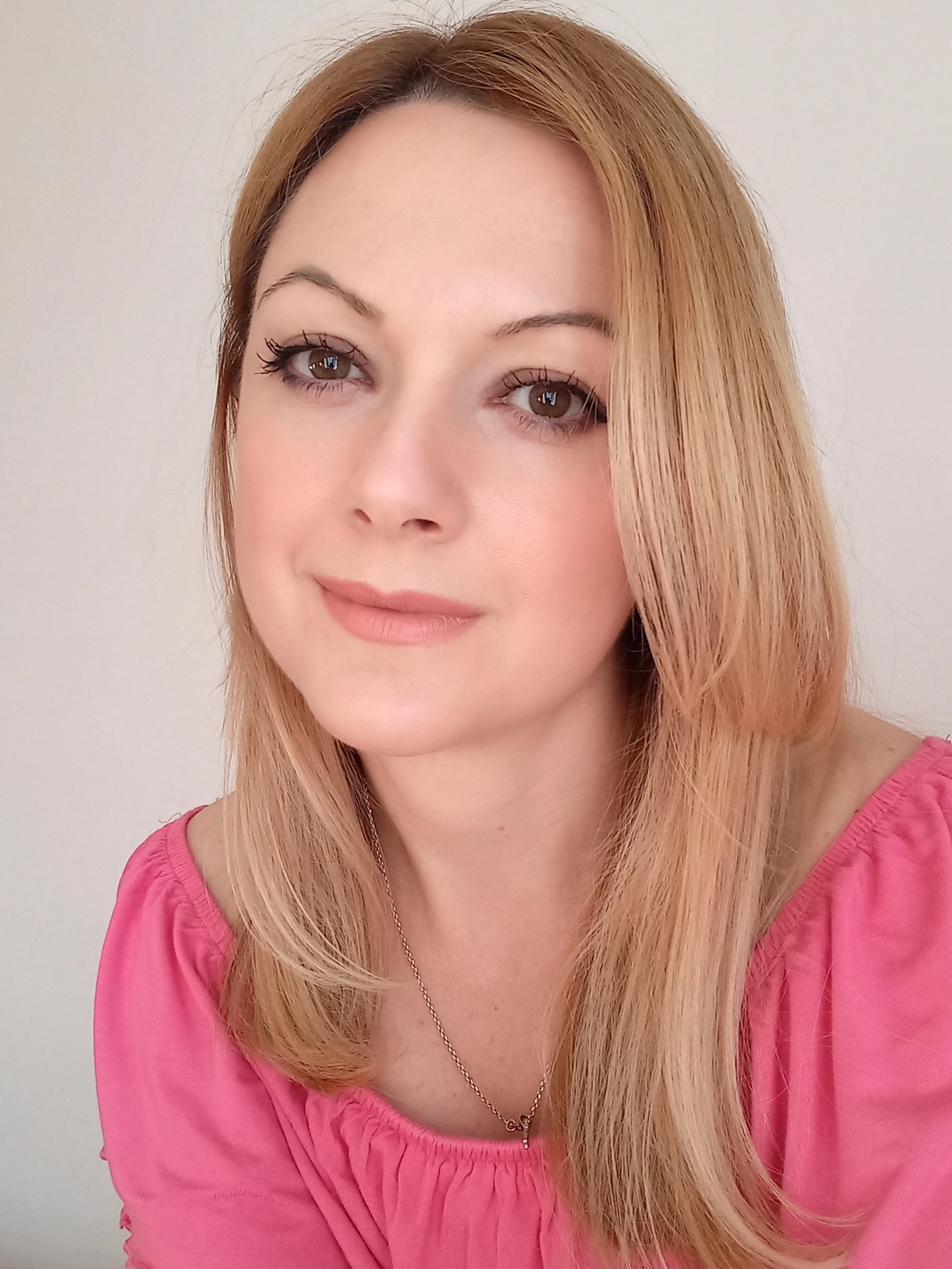 Portrait of a woman with blonde hair, brown eyes and a pink blouse.